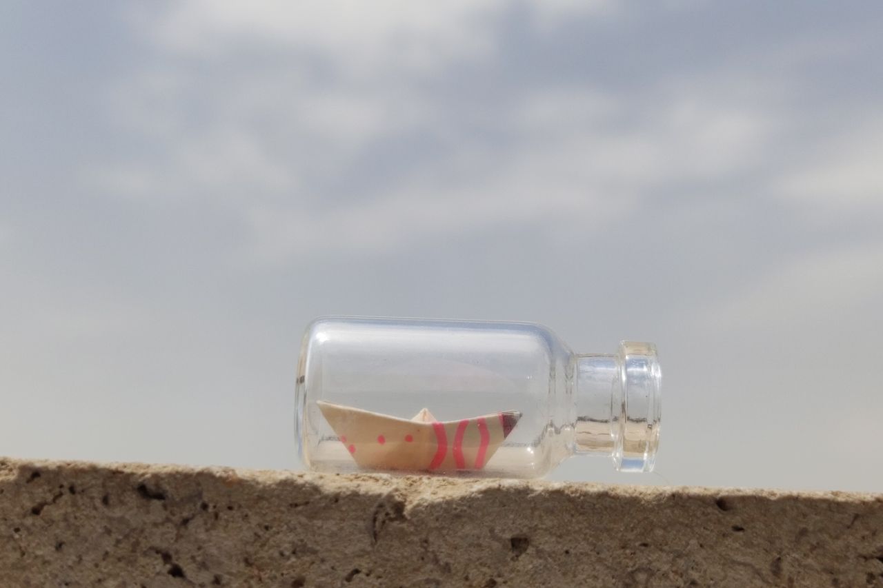 A glass bottle with a miniature paper boat against a clear sky. Conceptual outdoor art.