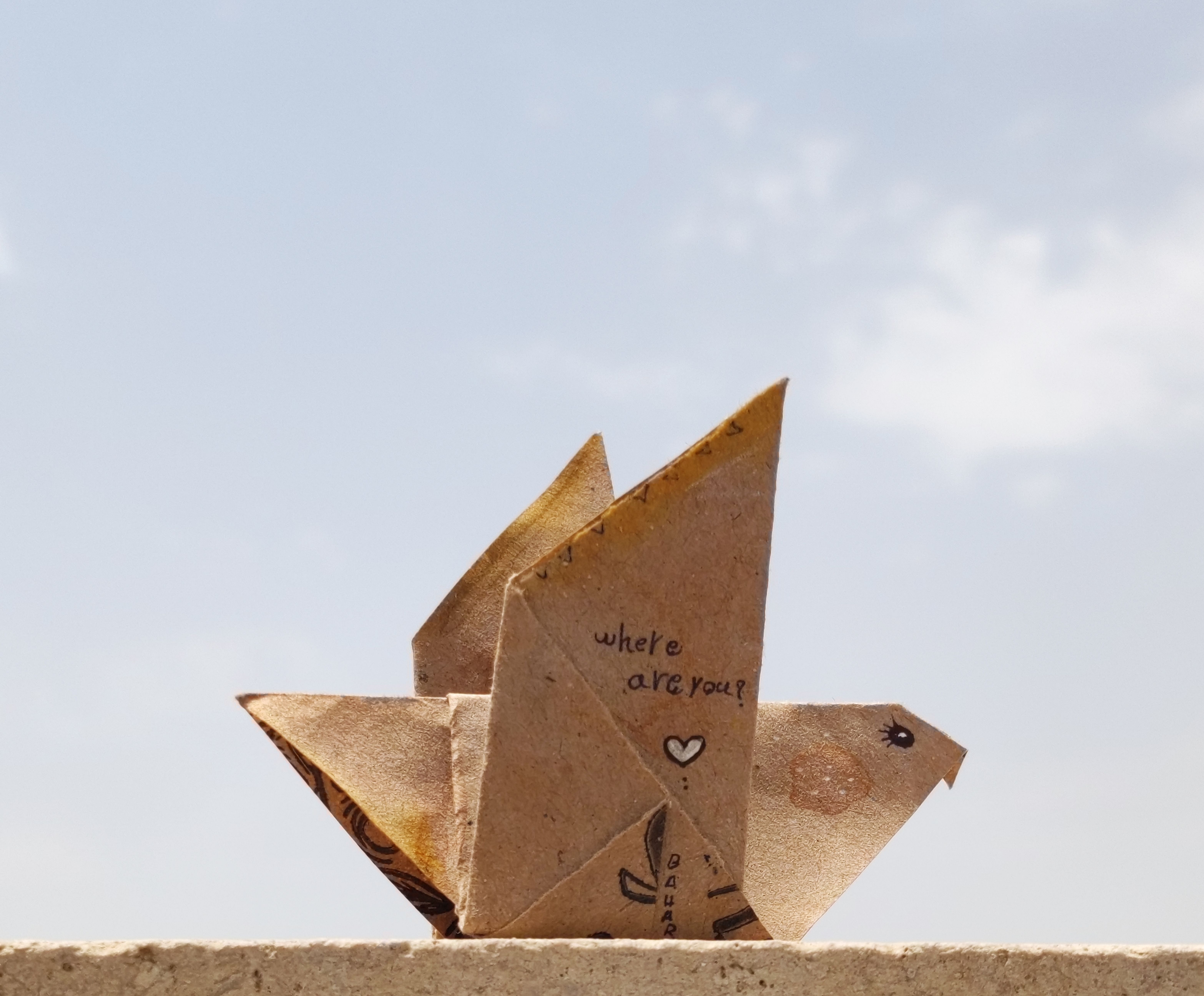 A creatively folded paper bird with text 'where are you?' against a clear blue sky.