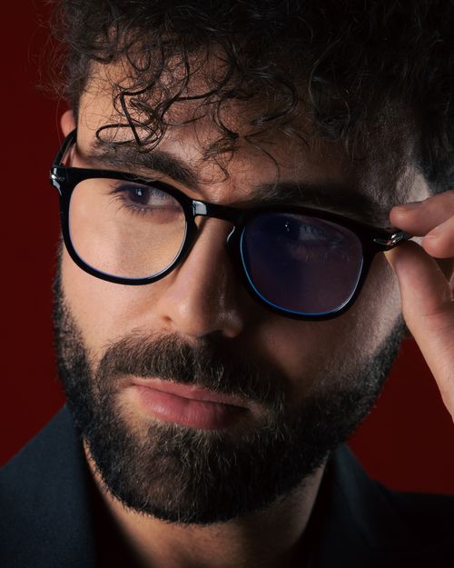 Free Close-up of a man with curly hair adjusting glasses against a red background. Stock Photo