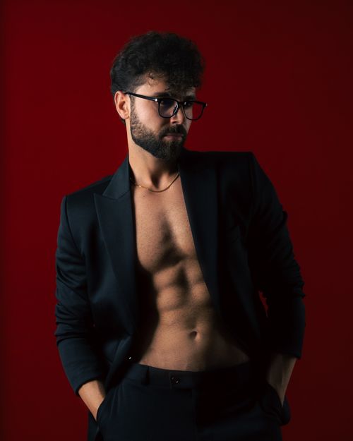 Free Stylish man in an open blazer posing confidently against a bold red backdrop. Stock Photo