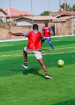 Two men playing soccer on an outdoor field, engaging in action sports with vibrant jerseys.