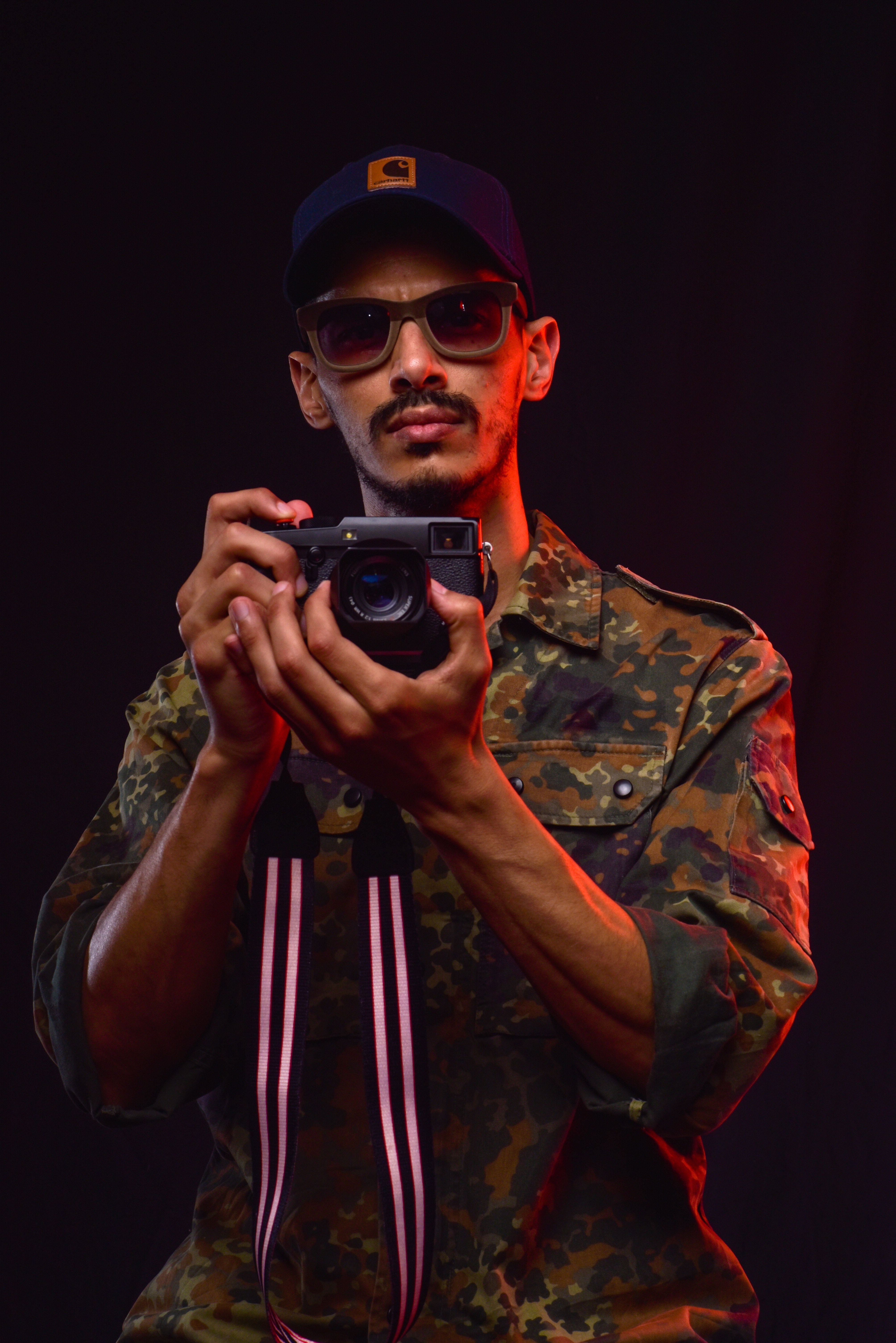 Man in sunglasses and camouflage jacket taking a photograph with a camera.