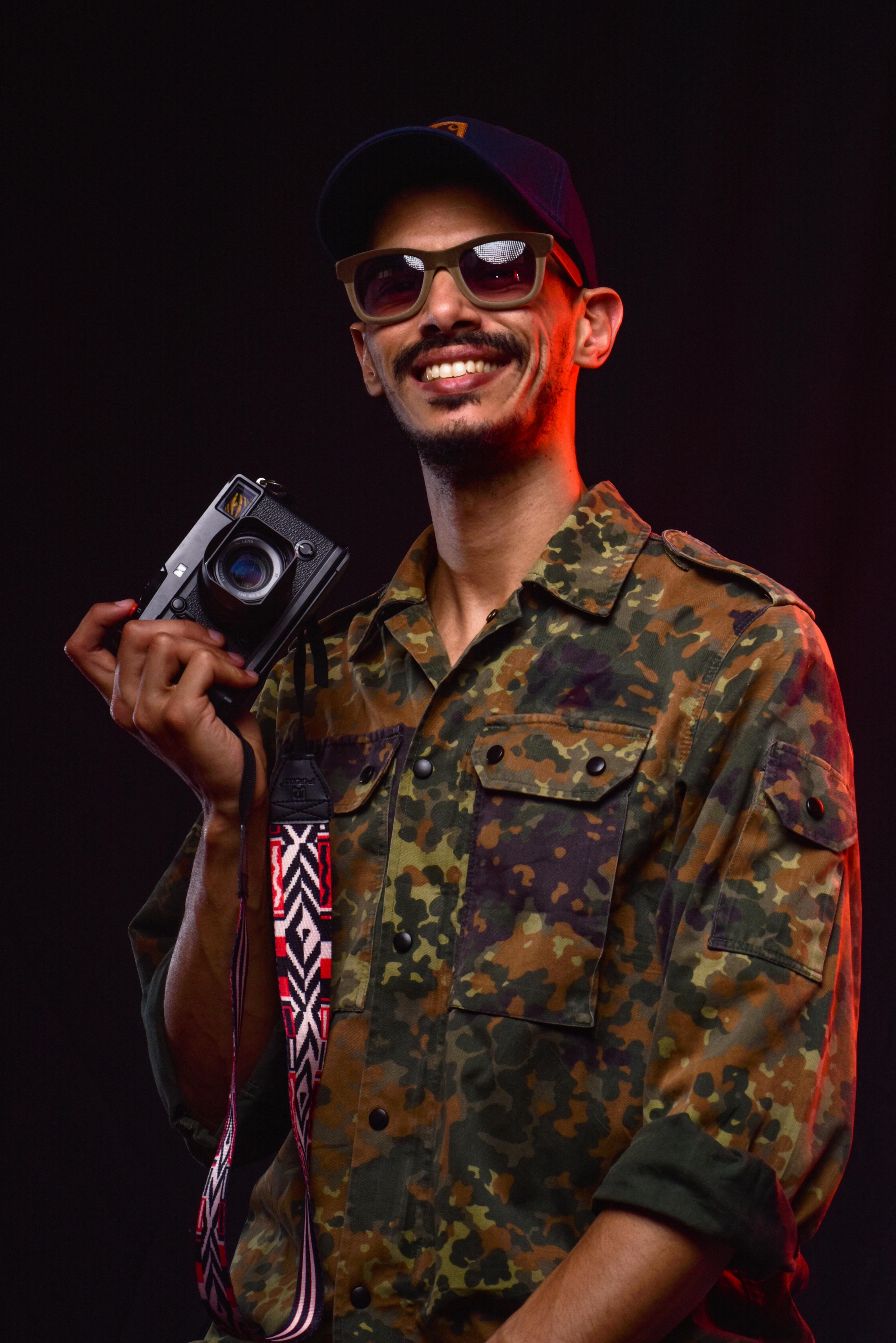 Young male photographer in sunglasses holding a vintage camera and smiling