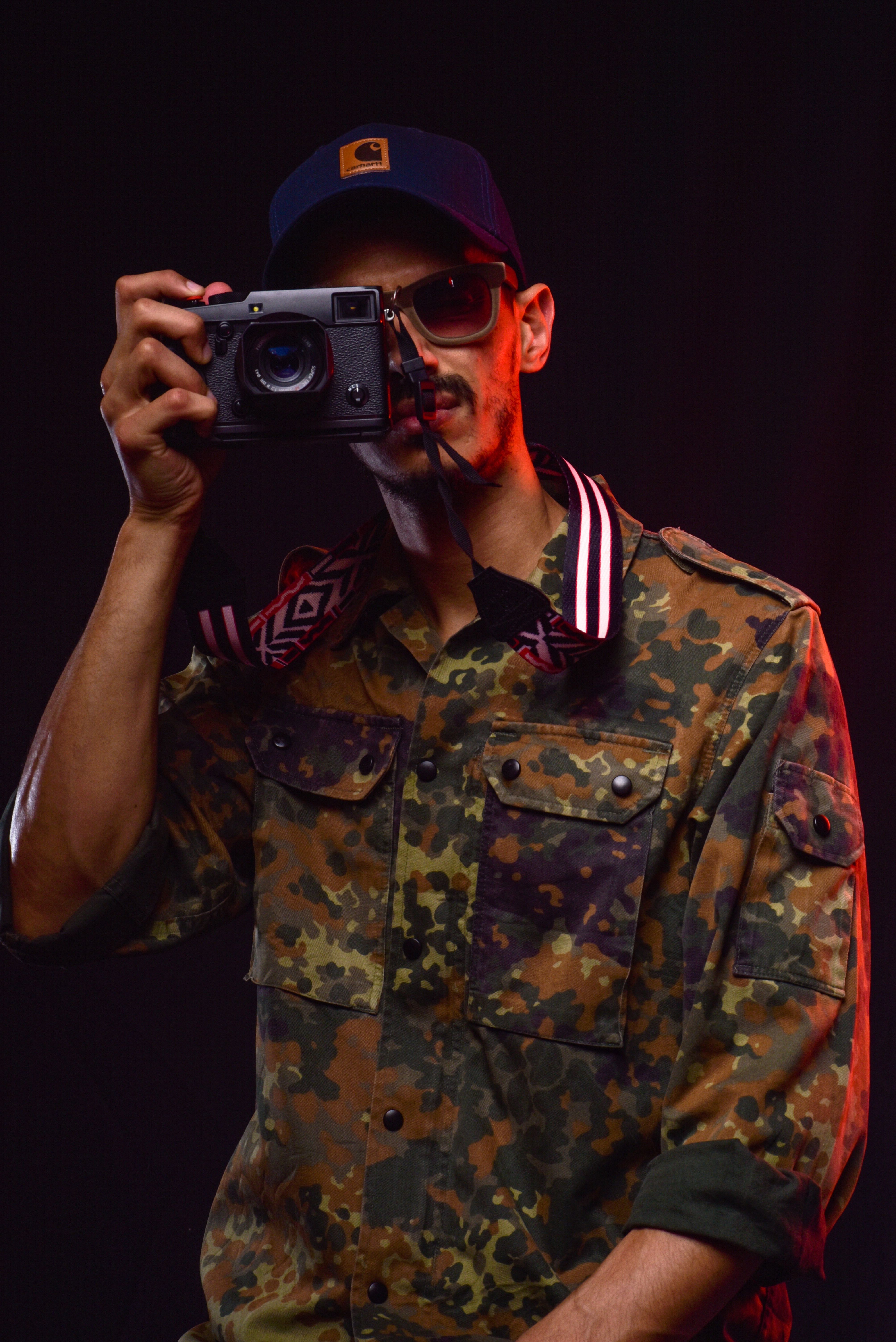 Dynamic portrait of a photographer in a camouflage jacket and cap, holding a camera.