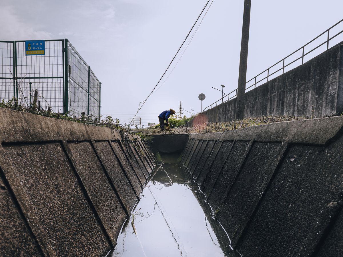 A worker in blue clothing checking a large concrete drainage channel