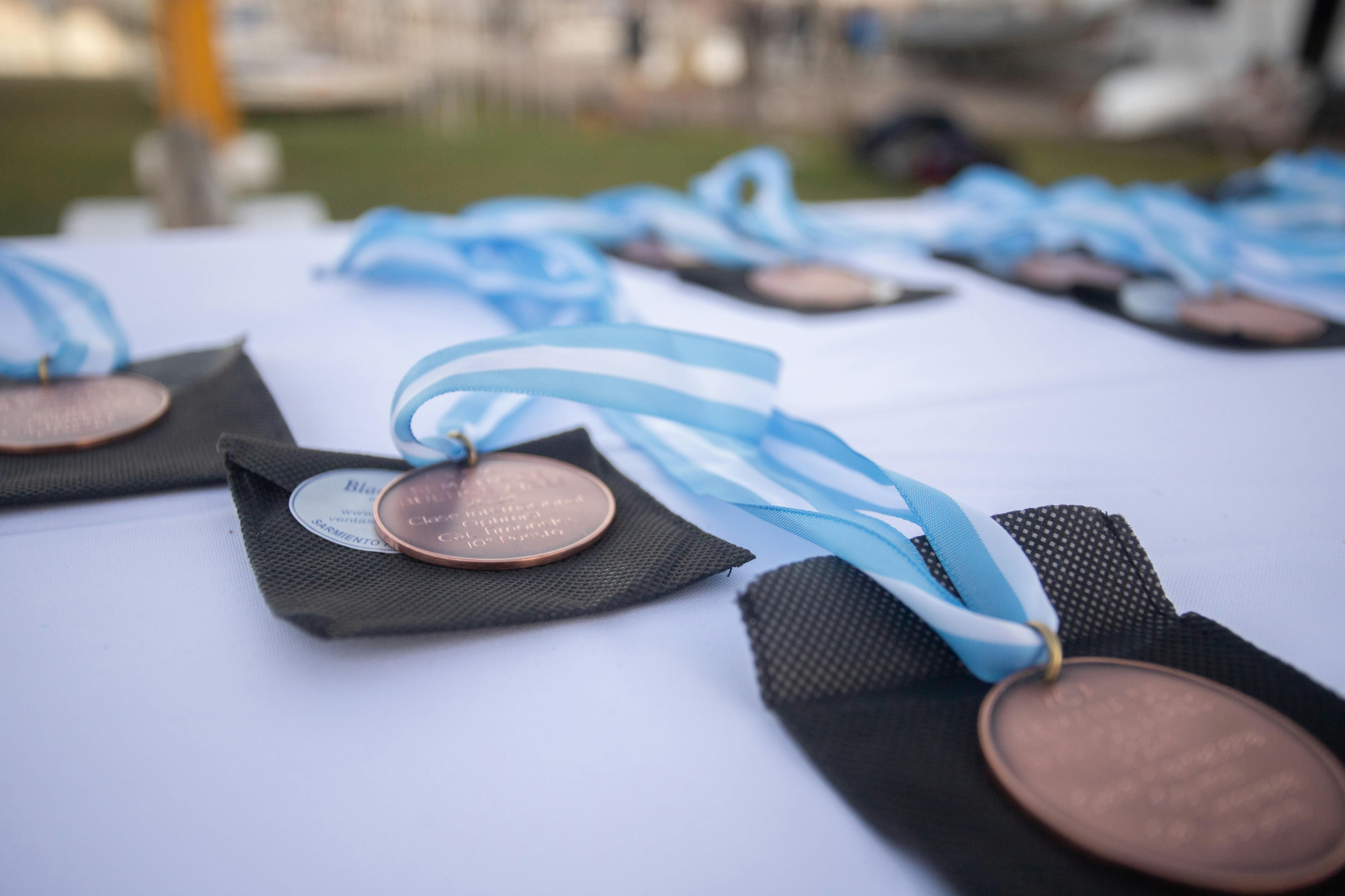 Close-up of bronze medals with blue ribbons laid out on a table at an outdoor ceremony in Mar del Plata, Argentina.