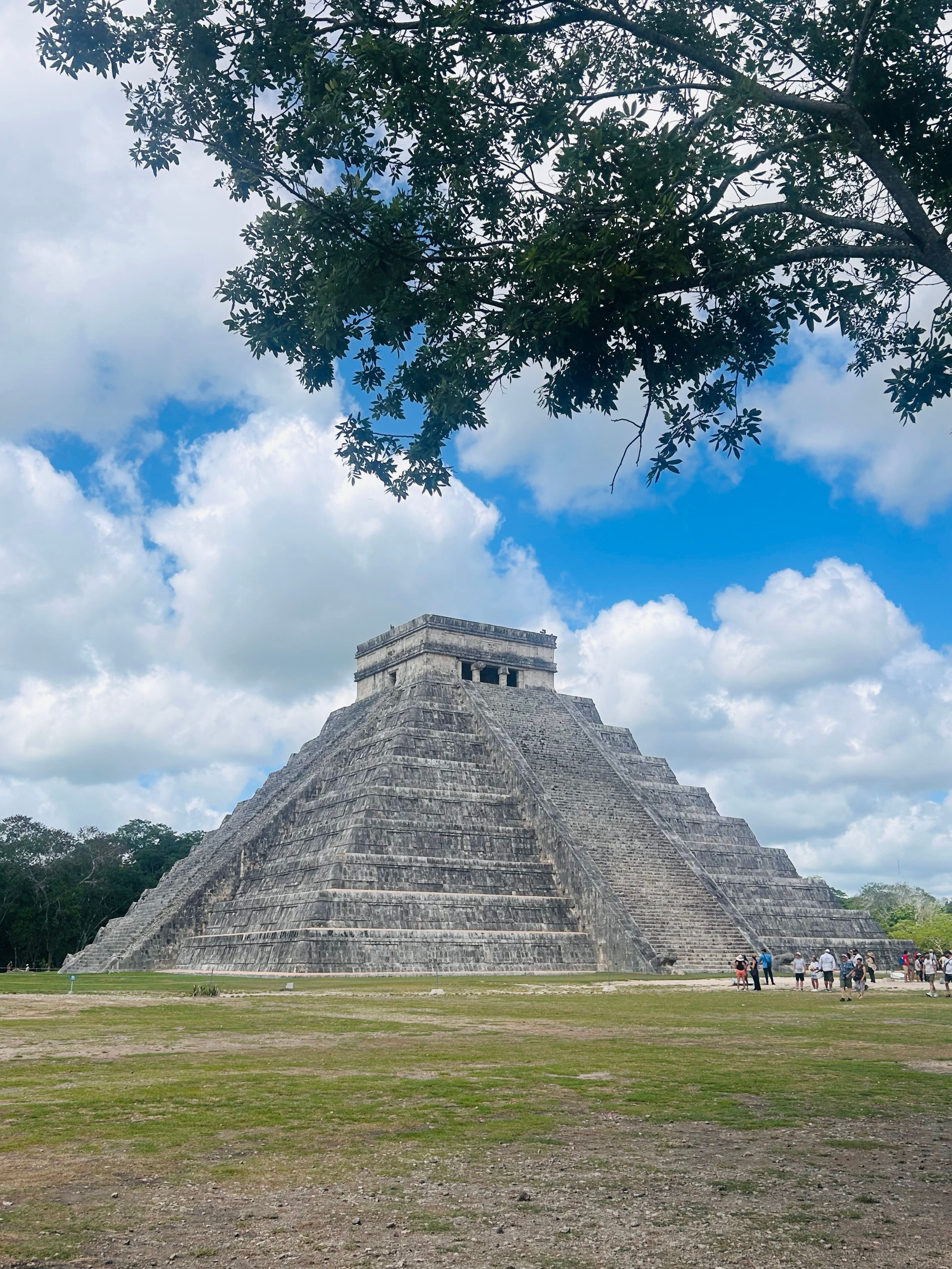 El Castillo pyramid at Chichén Itzá under a blue sky with visitors at the base of the Mayan site
