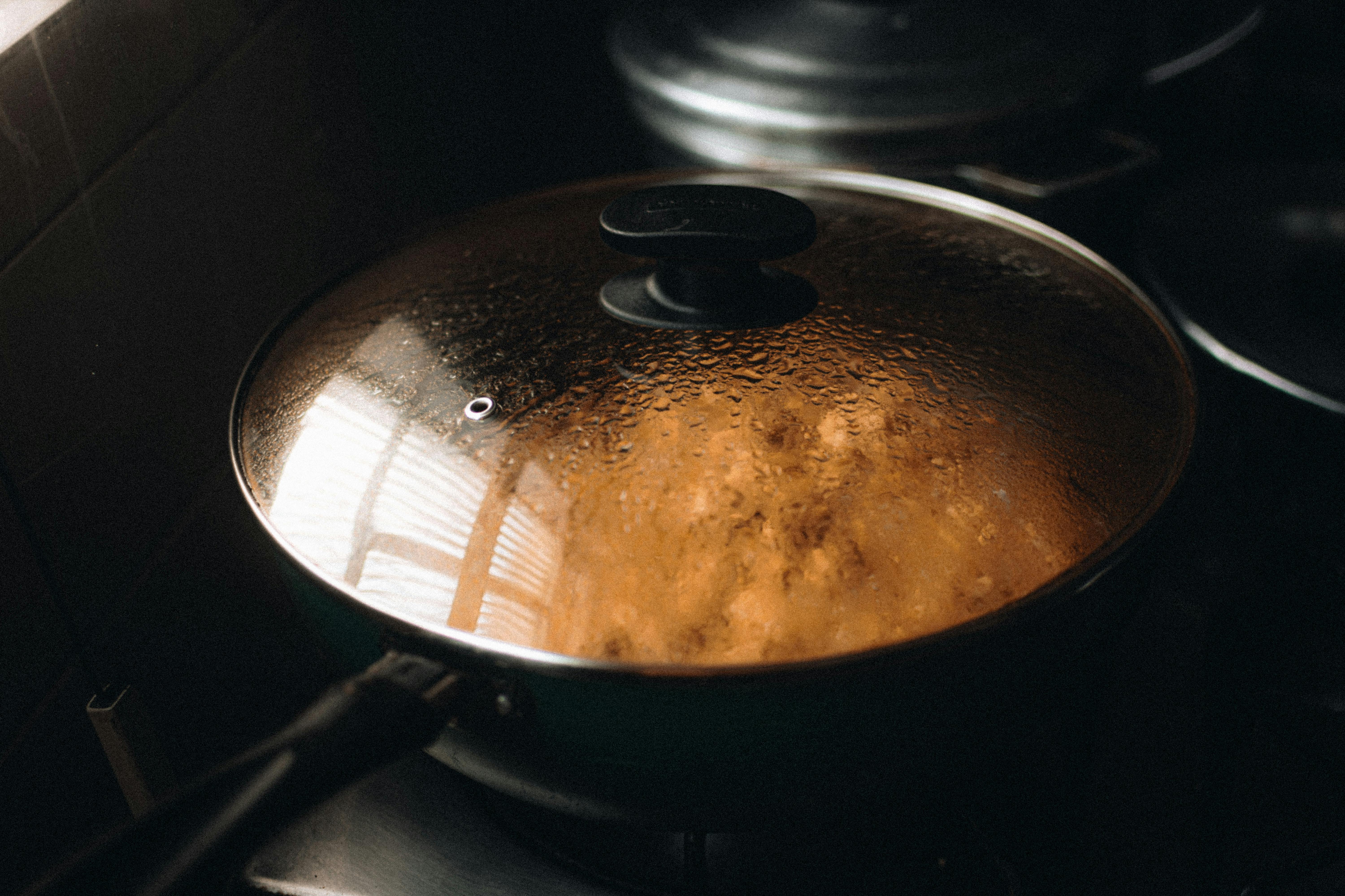 Close-up of a steaming lidded pan on a stovetop, illustrating home cooking ambiance.