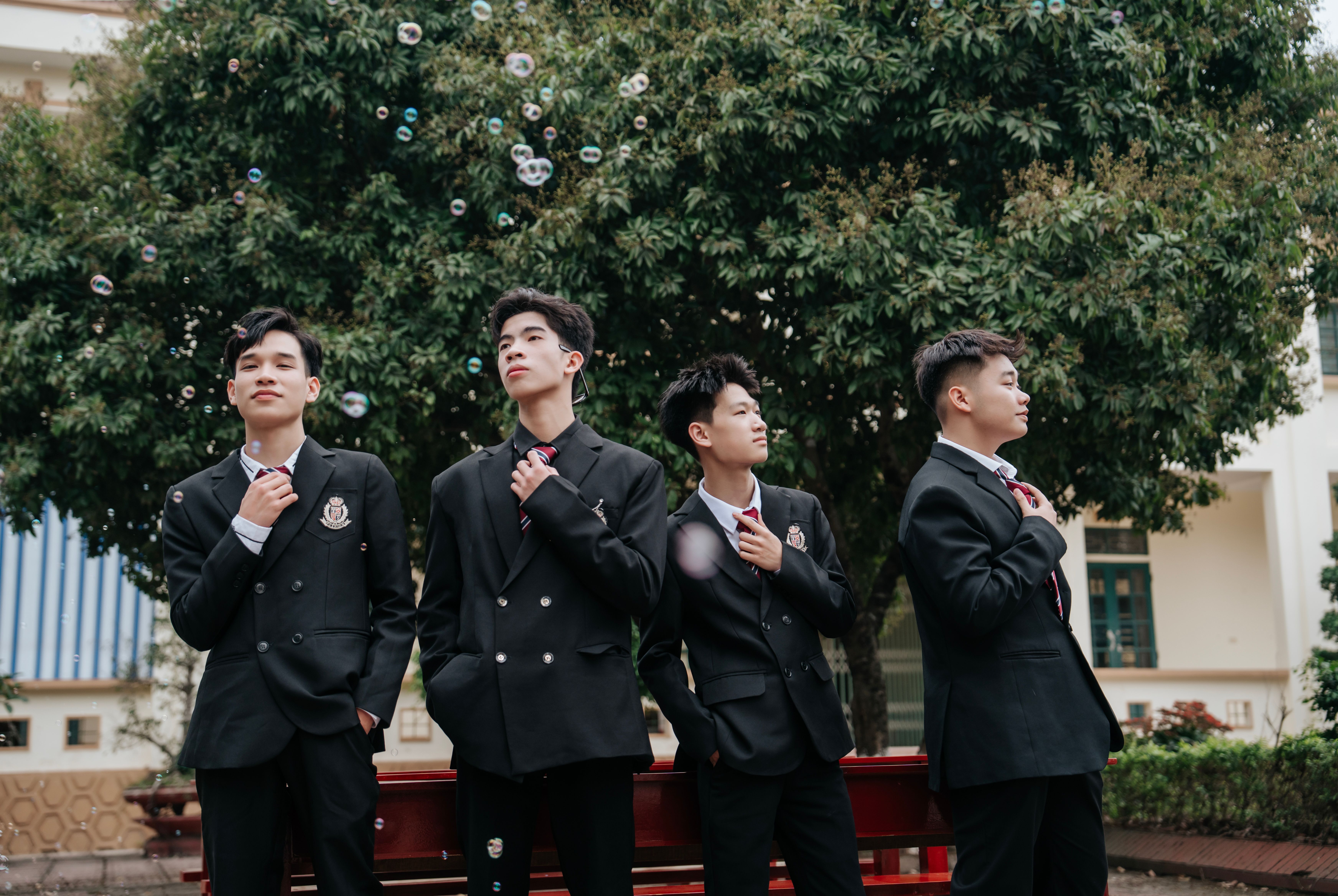 Four young men in suits posing confidently outdoors, surrounded by bubbles.
