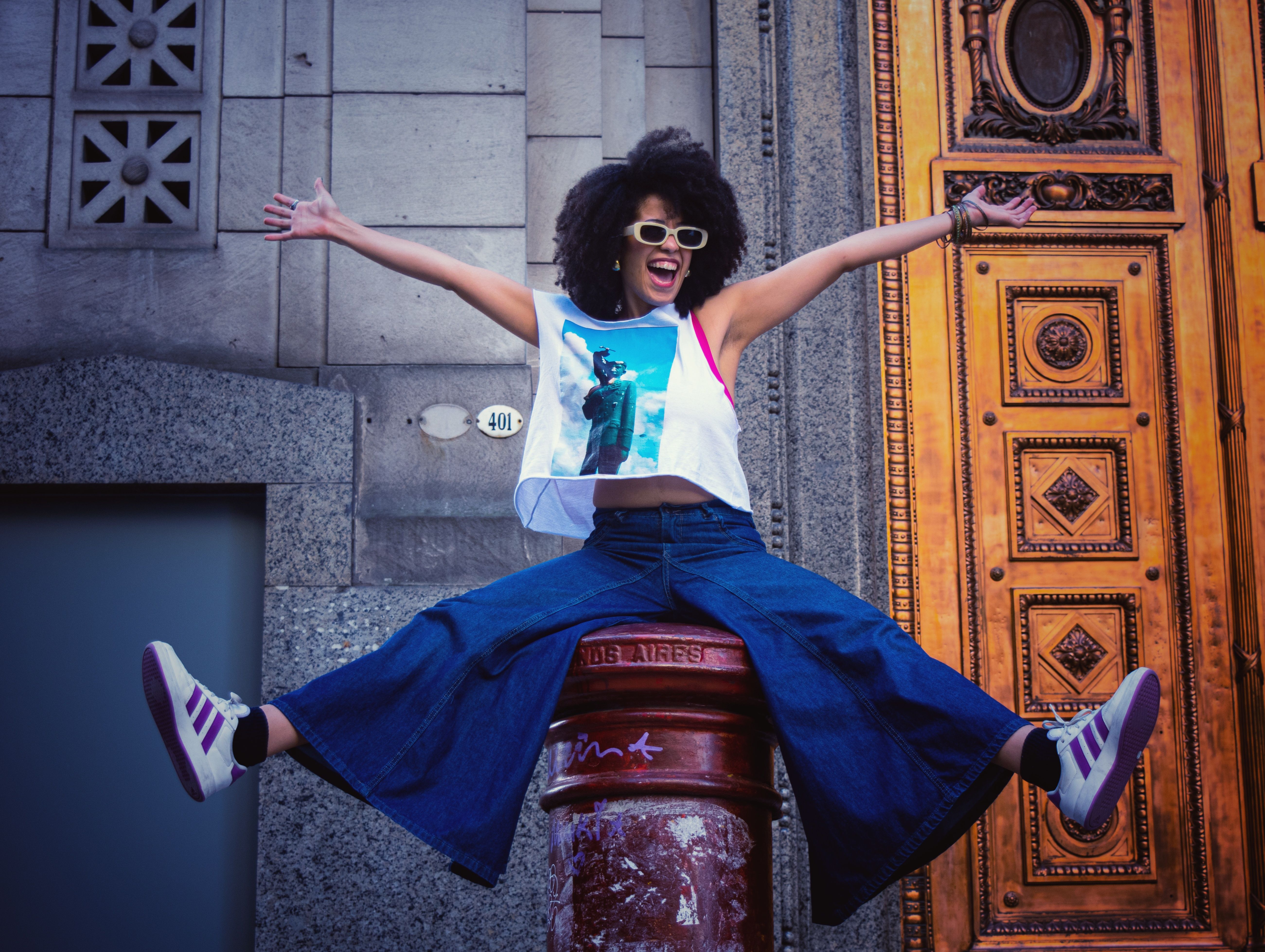 A cheerful woman in urban attire jumps energetically in a vibrant cityscape.