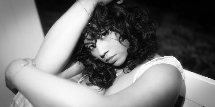 Ritratto ravvicinato in bianco e nero di una donna con i capelli ricci e un anello al naso in posa rilassata.