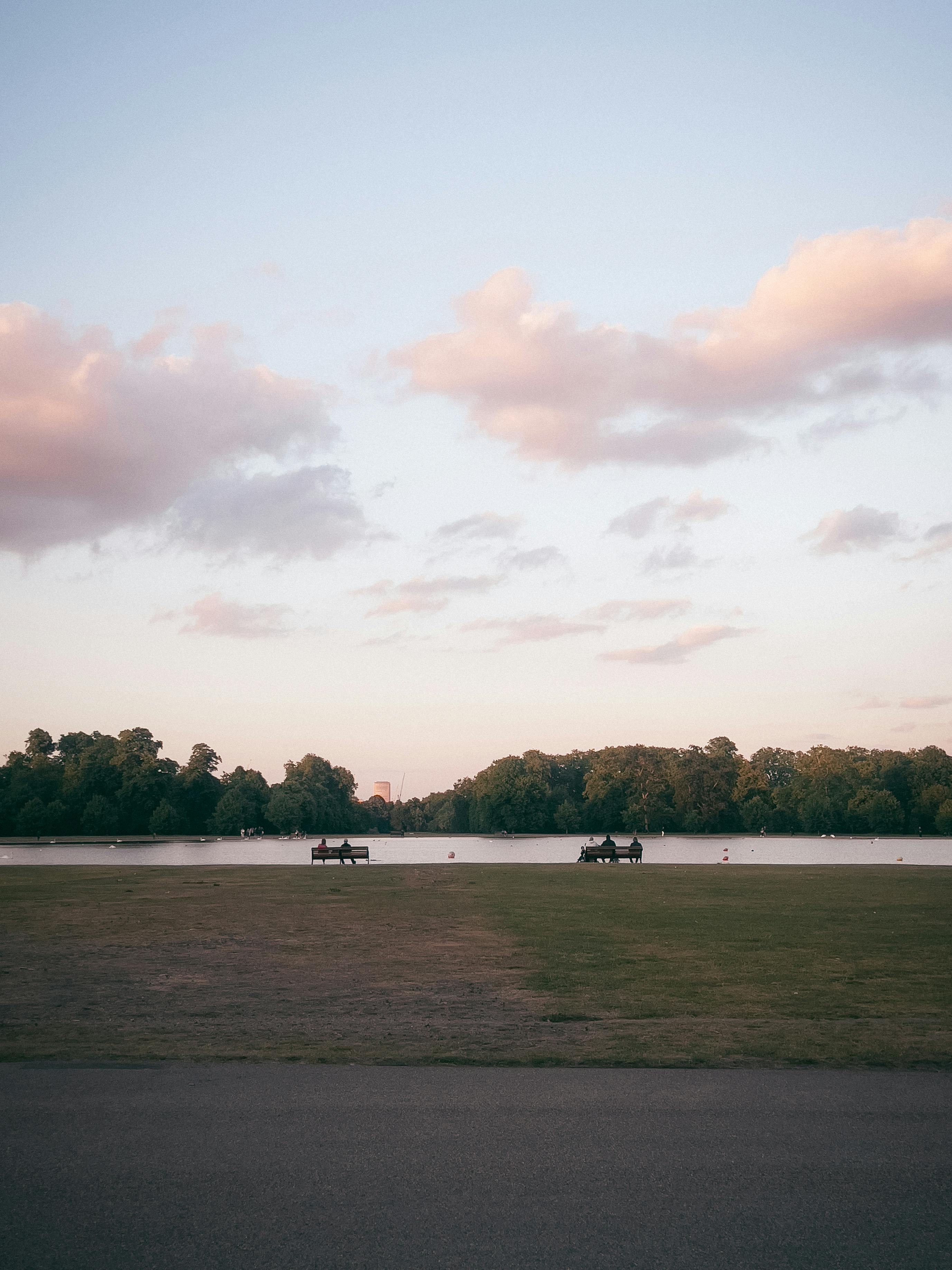 A tranquil park scene with benches overlooking a lake during sunset.