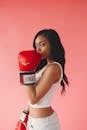 一位时尚女子戴着红色拳击手套，在粉色背景前摆出自信健康的姿势