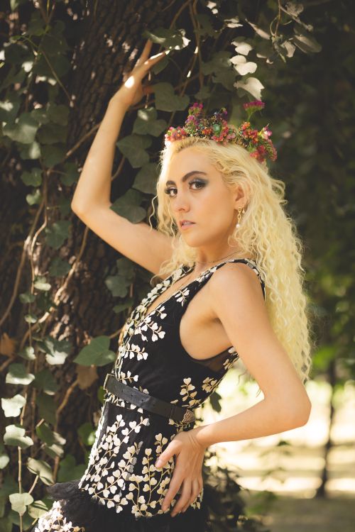 Free Blonde woman in black dress with flower crown posing gracefully outdoors. Stock Photo