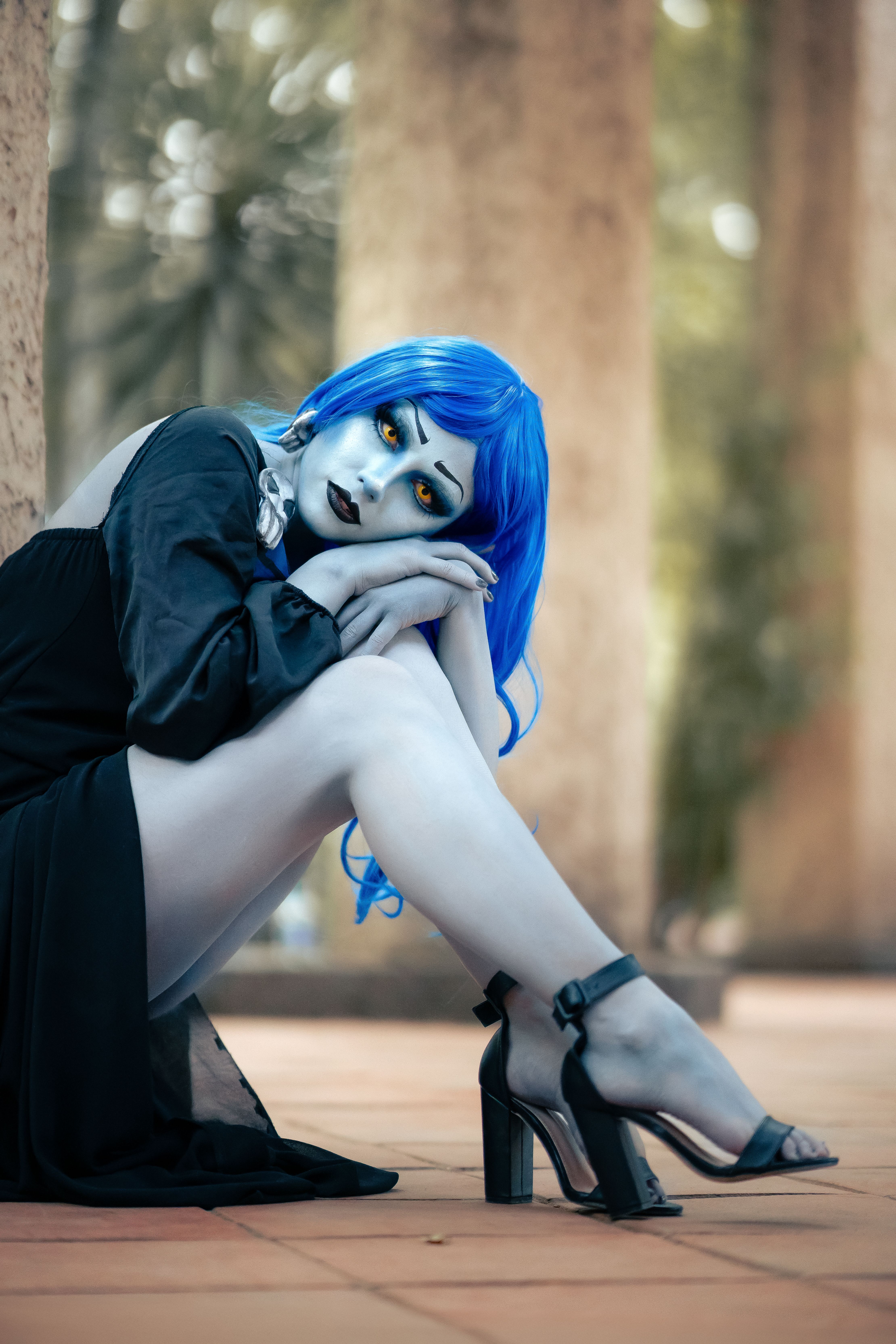 A fantasy-themed portrait of a woman with striking blue hair and vivid eyes in an outdoor setting.