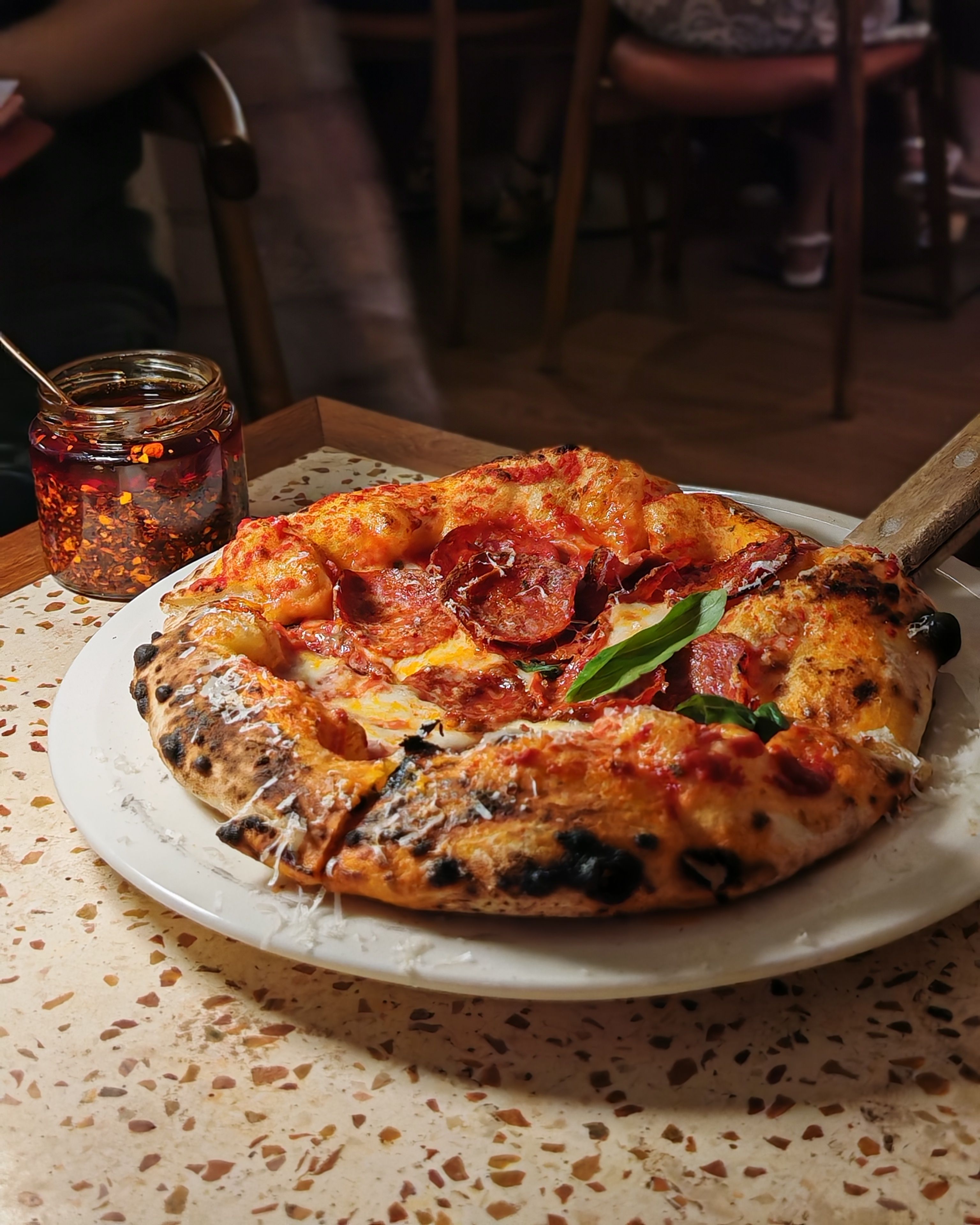 Appetizing pepperoni pizza on a table with chili flakes, perfect for a cozy dining experience.
