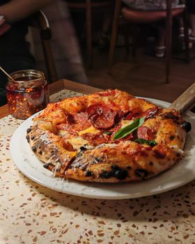 Appetizing pepperoni pizza on a table with chili flakes, perfect for a cozy dining experience.