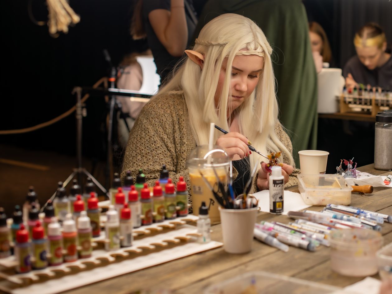 Fyreslayers Lose Seven Entries to Legends, and Owners Get a 12-Month Clock A woman dressed as an elf paints miniatures at an indoor convention table