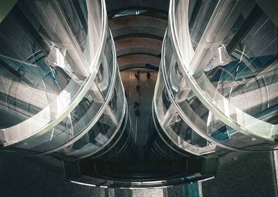 Aerial view of a modern glass elevator shaft with people below, showcasing architectural innovation.