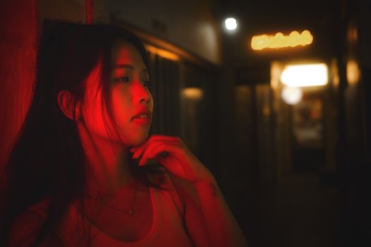Stylized portrait of a woman under red neon light in a dimly lit corridor.