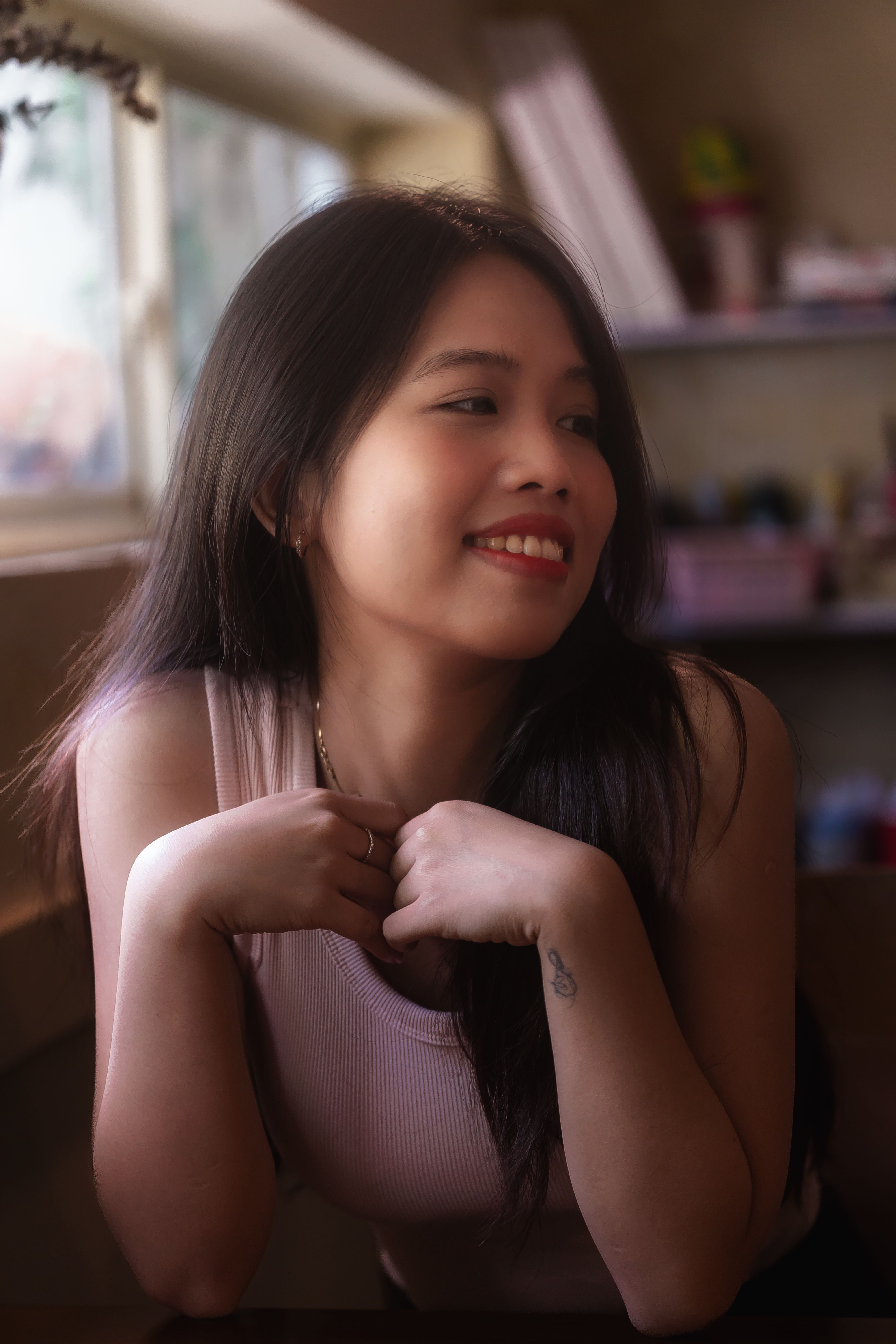Young woman smiling and relaxing indoors by sunlight through a window.