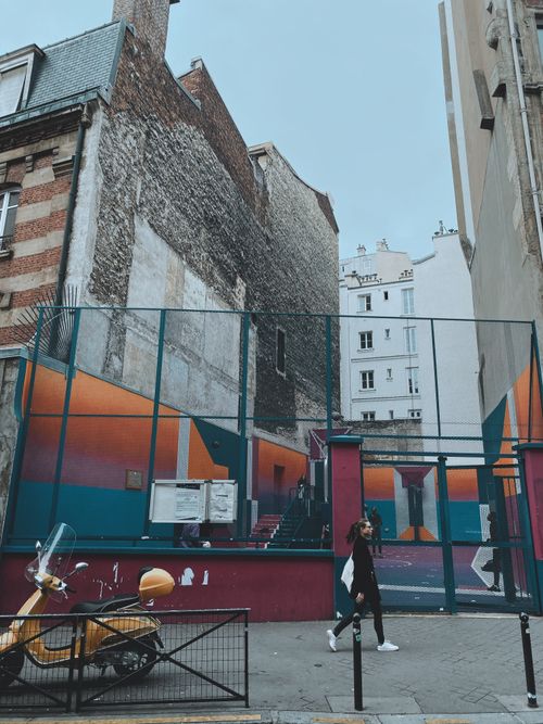 Free Woman walking past a vibrant playground in a Paris street, showcasing urban life. Stock Photo