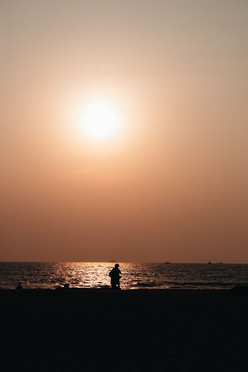 Free A tranquil sunset over the ocean with a silhouette on the beach, capturing the day's end. Stock Photo
