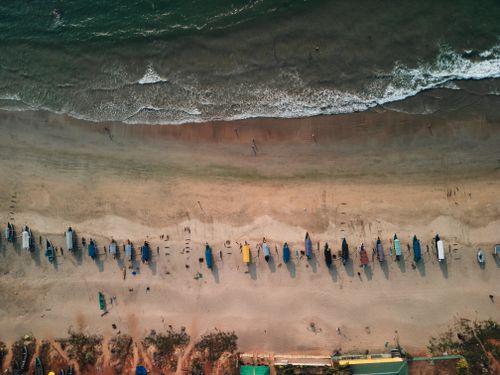 Free An aerial shot showcasing colorful boats lined up on a sandy beach with gentle waves touching the shore. Stock Photo