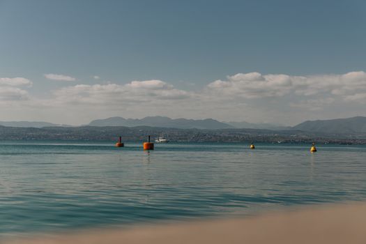 Serene view of Lake Garda with distant mountains and buoys under a sunny sky.