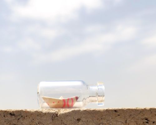 Free A small paper boat inside a clear glass bottle resting on a wall under a bright sky. Stock Photo