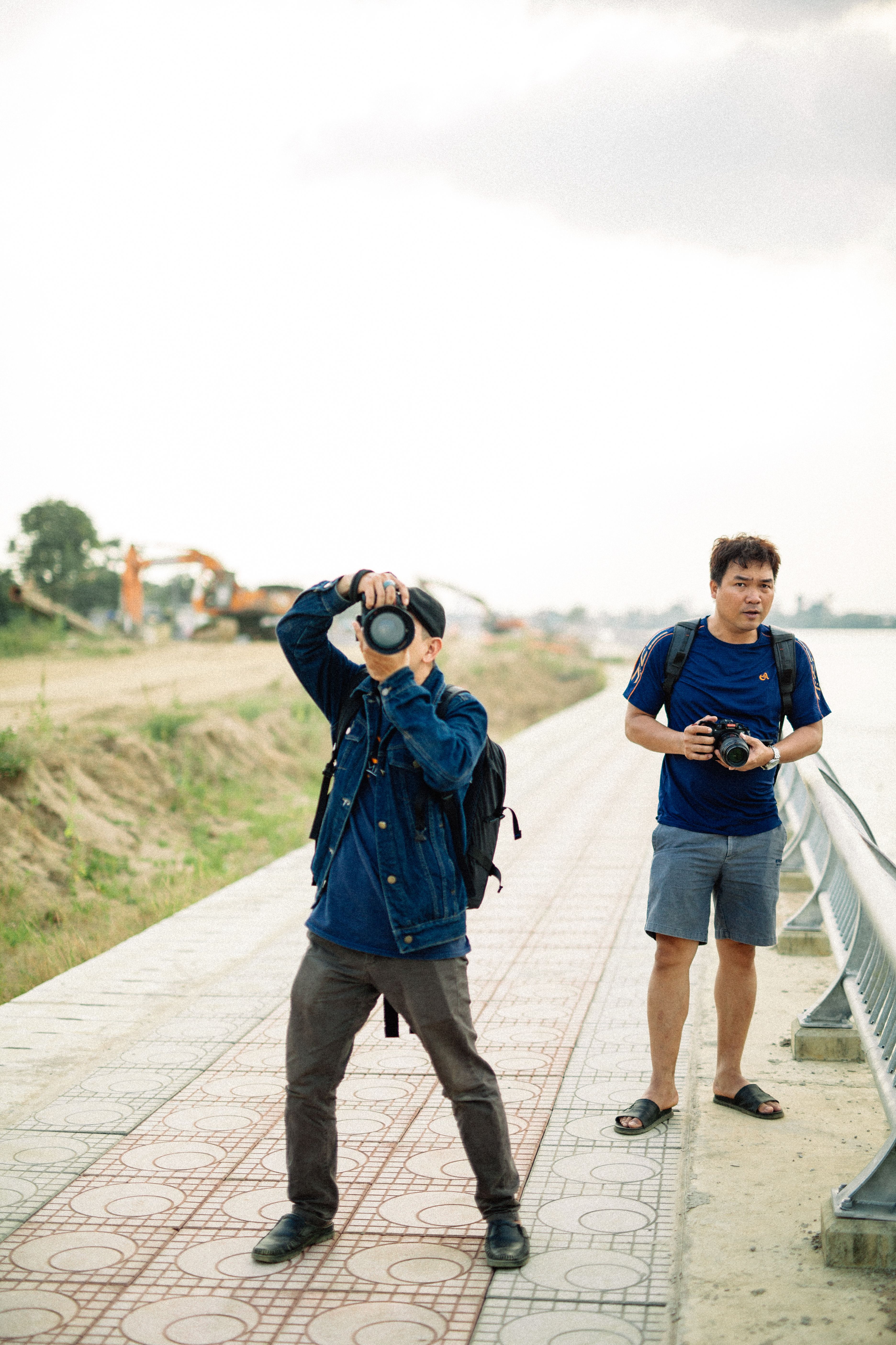 Two photographers taking photos by a riverside walkway on a cloudy day.