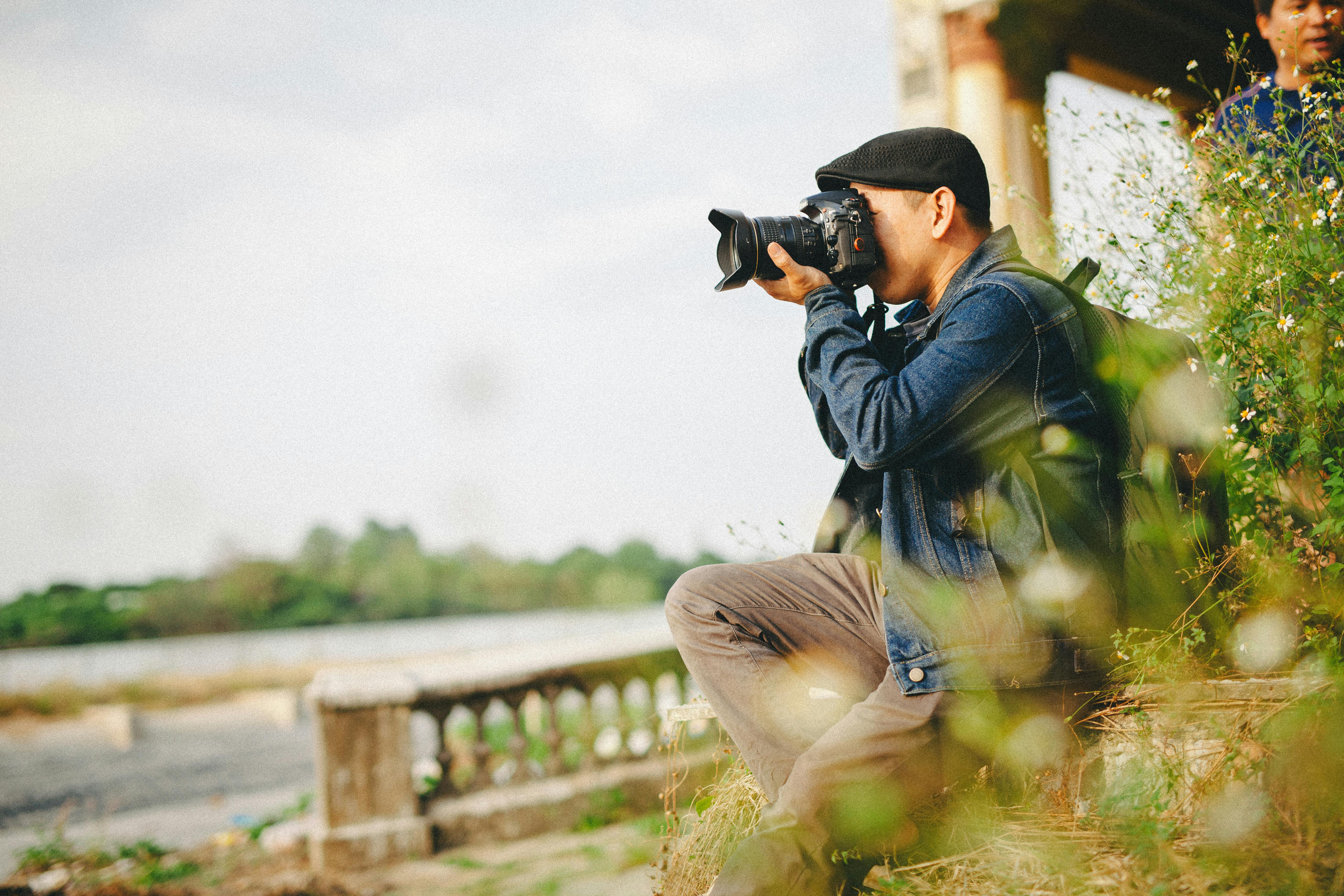 Photographer focusing on landscape with DSLR, surrounded by nature.