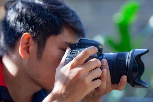 An adult male photographer takes a picture with his DSLR camera outdoors on a sunny day.