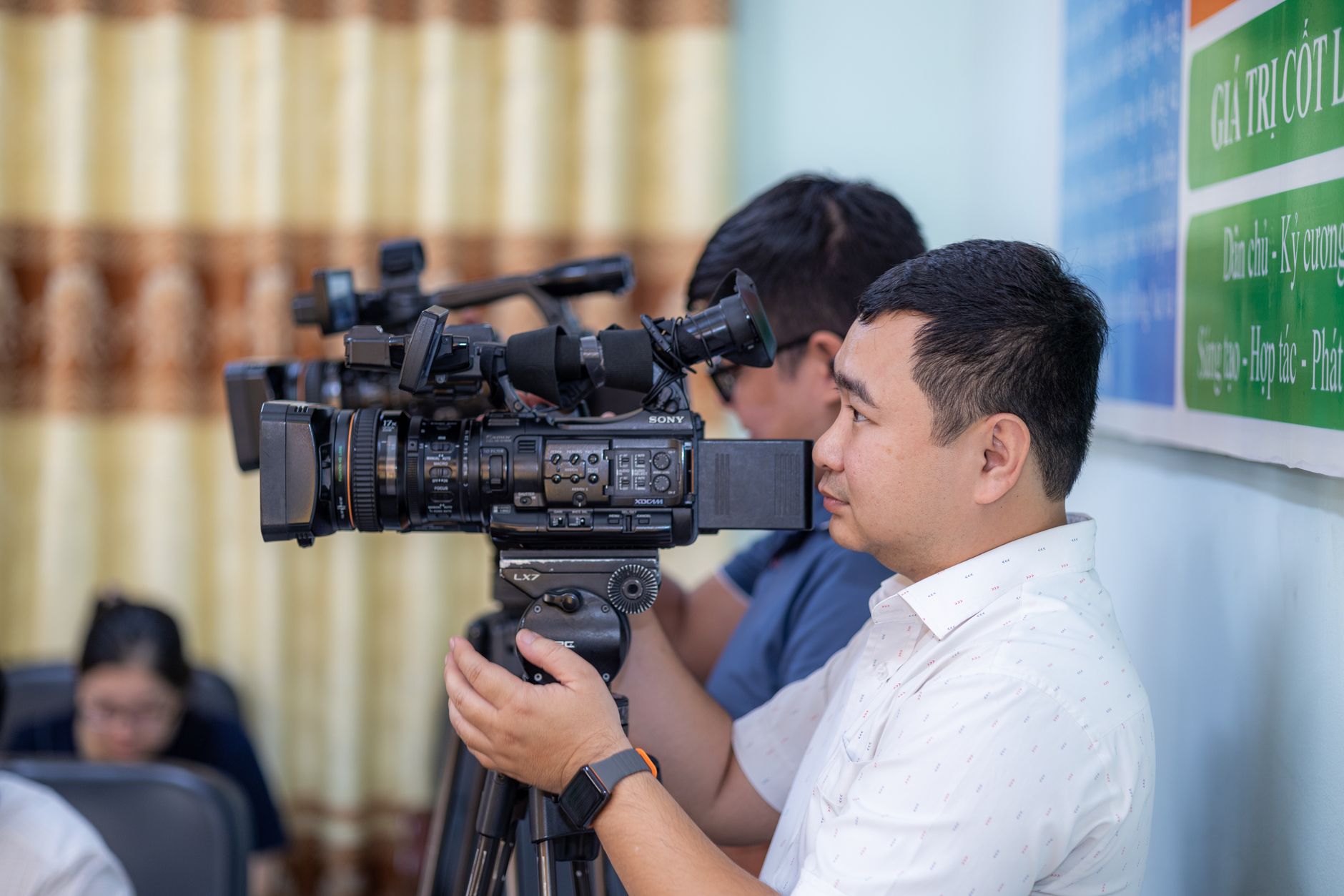 Male cameraman operating a professional video camera during an indoor event.