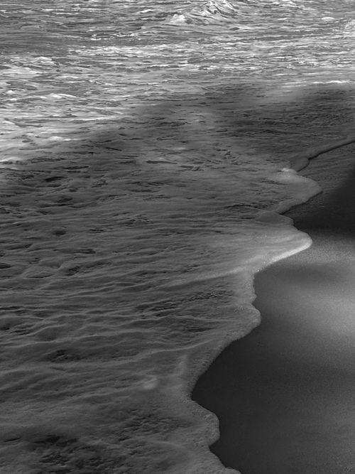 Free A dramatic black and white close-up of waves rolling onto a sandy beach. Stock Photo