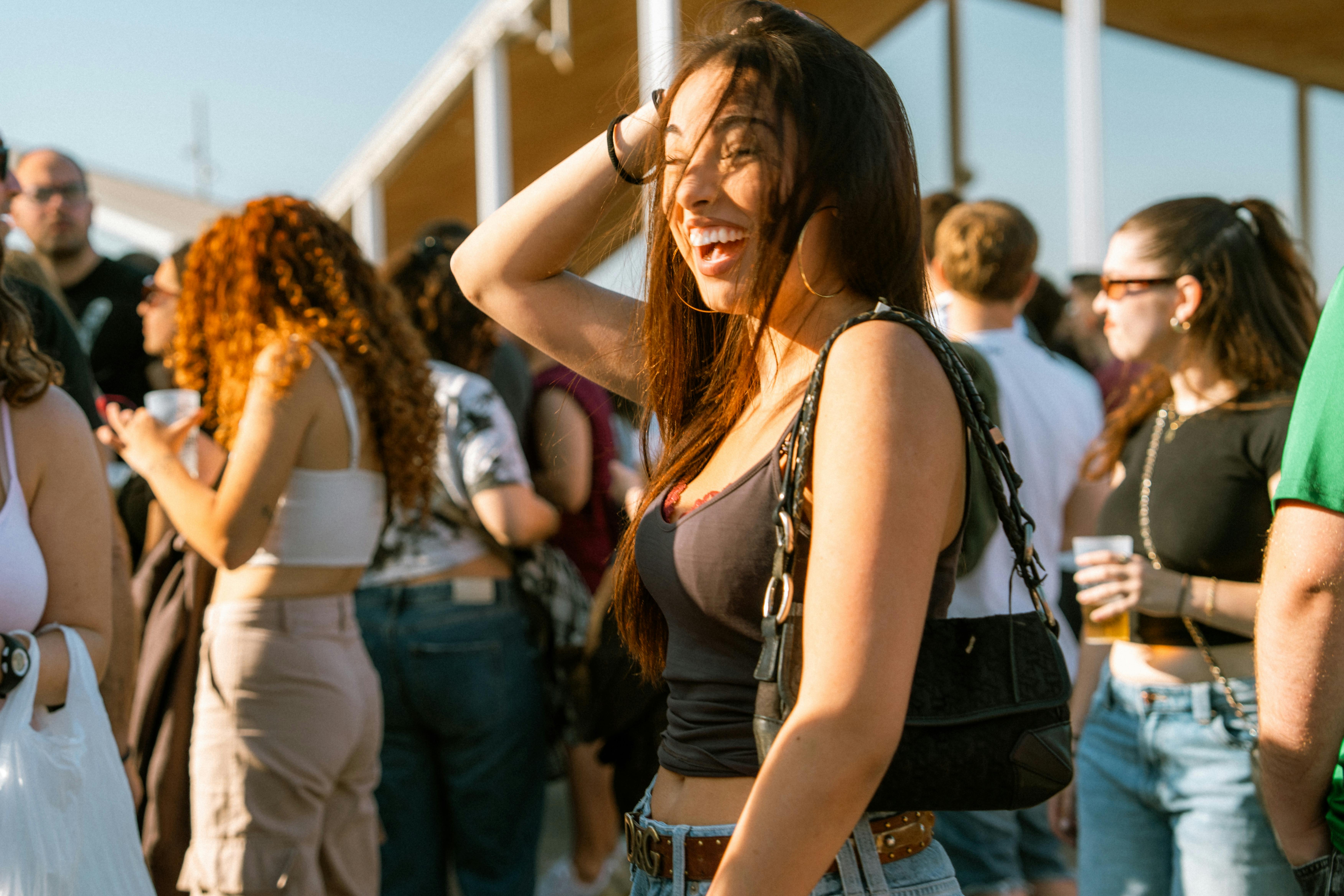 Young woman smiling at an outdoor festival with a lively crowd around.