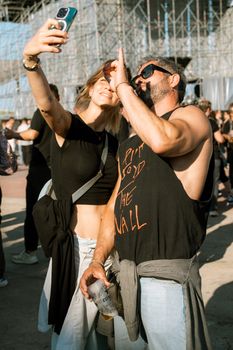 Two friends taking a selfie at an outdoor concert during the day.