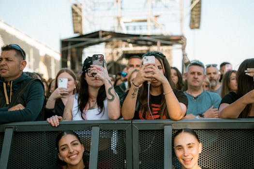 A lively crowd takes photos during an outdoor music concert on a sunny day.