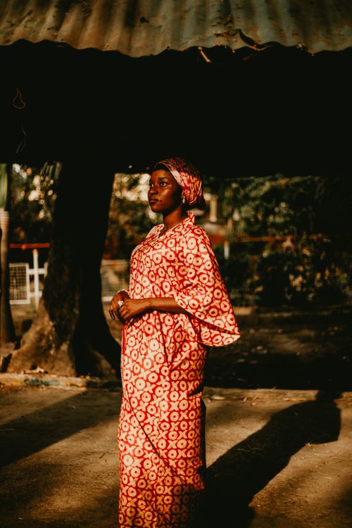 Free Woman in red patterned dress standing outside, illuminated by sunlight. Stock Photo