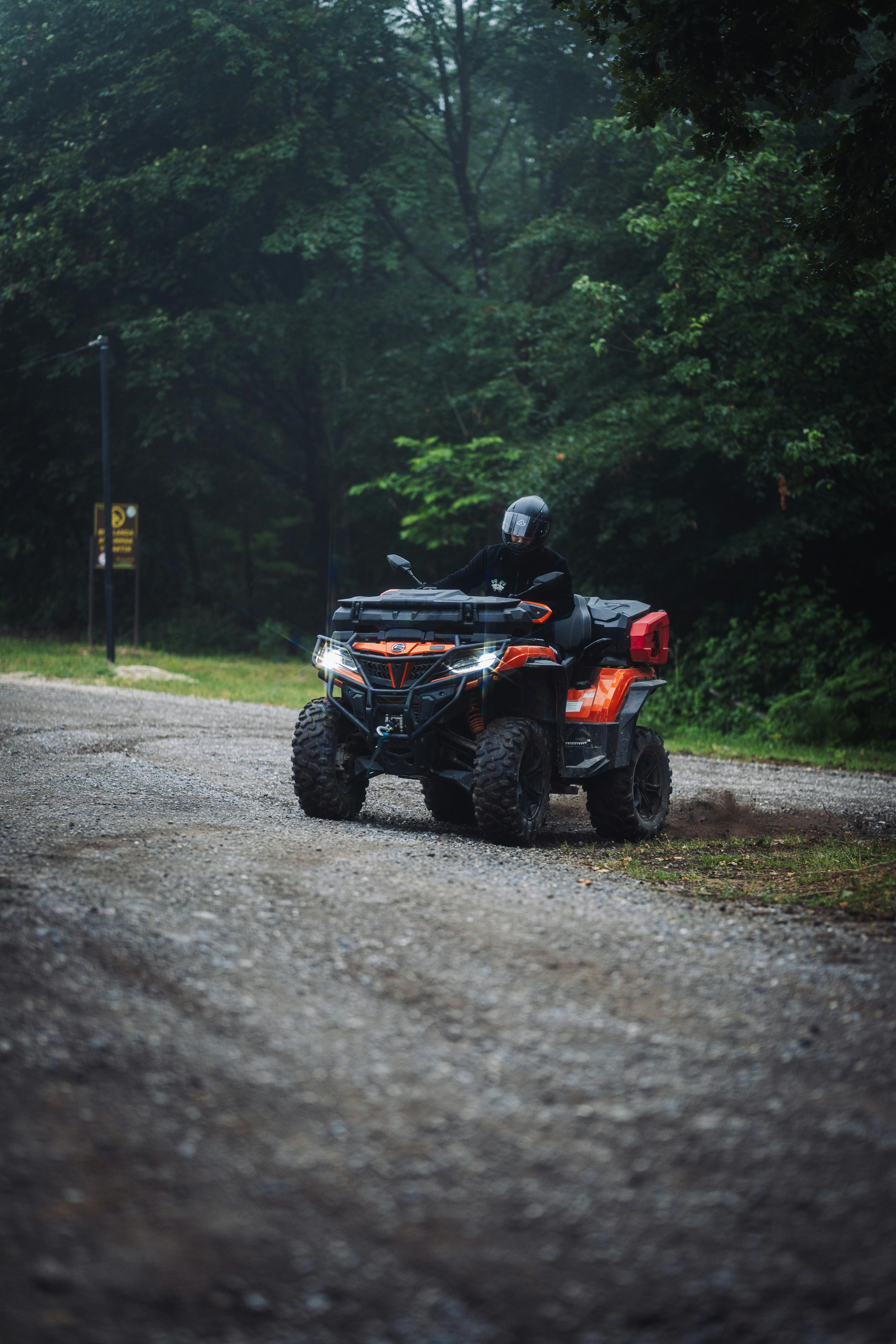 An ATV rider navigating a gravel path surrounded by lush green forest in misty conditions.