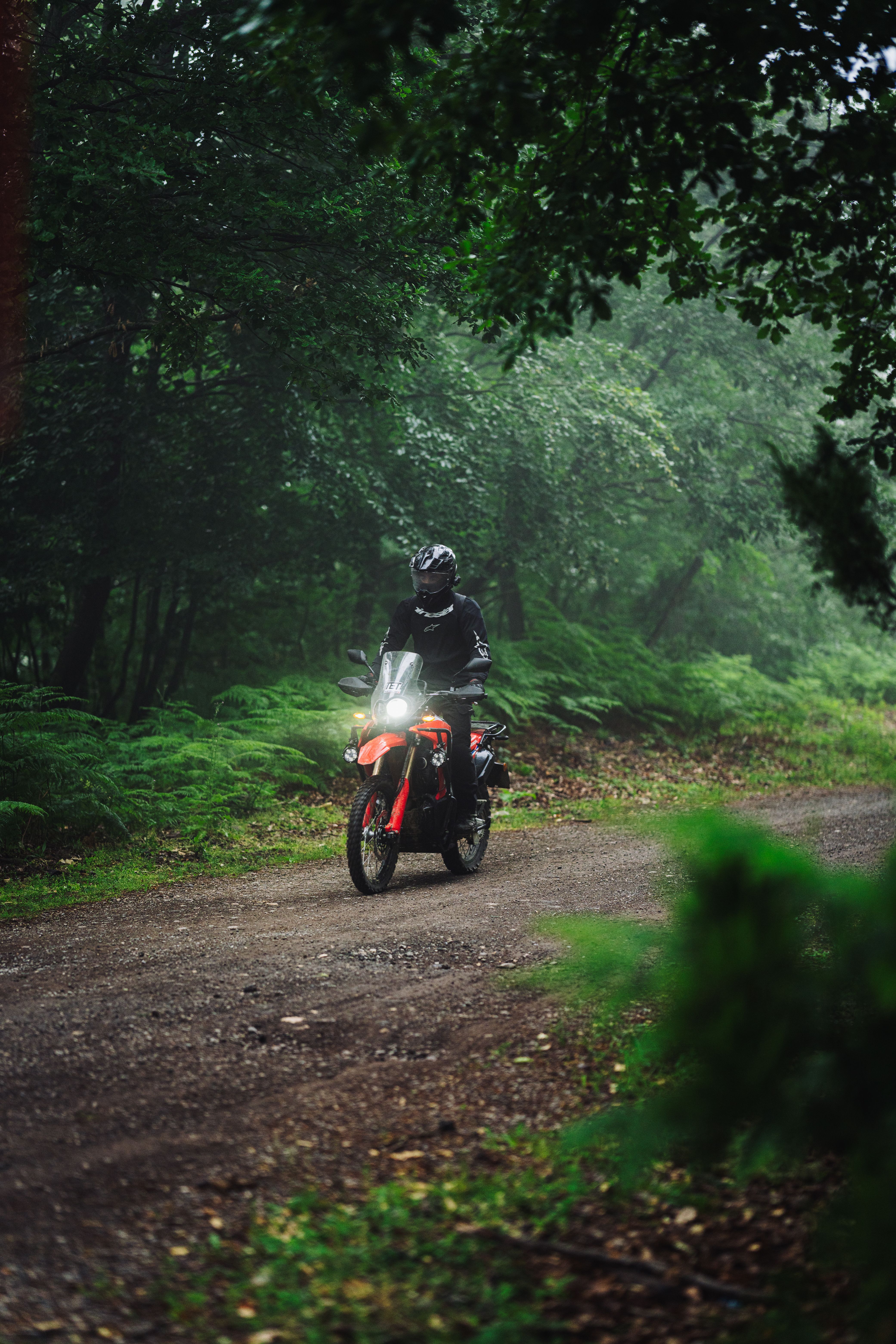 Adventurous motorcyclist navigating a dirt trail in a dense, green forest setting.