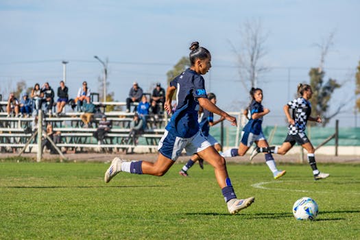 A woman dribbles the ball during a daytime soccer match, showcasing athletic skill and teamwork.