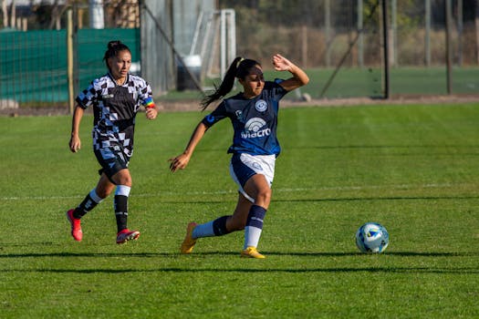 Action shot of female soccer players on a sunny outdoor field, capturing athleticism and competition.