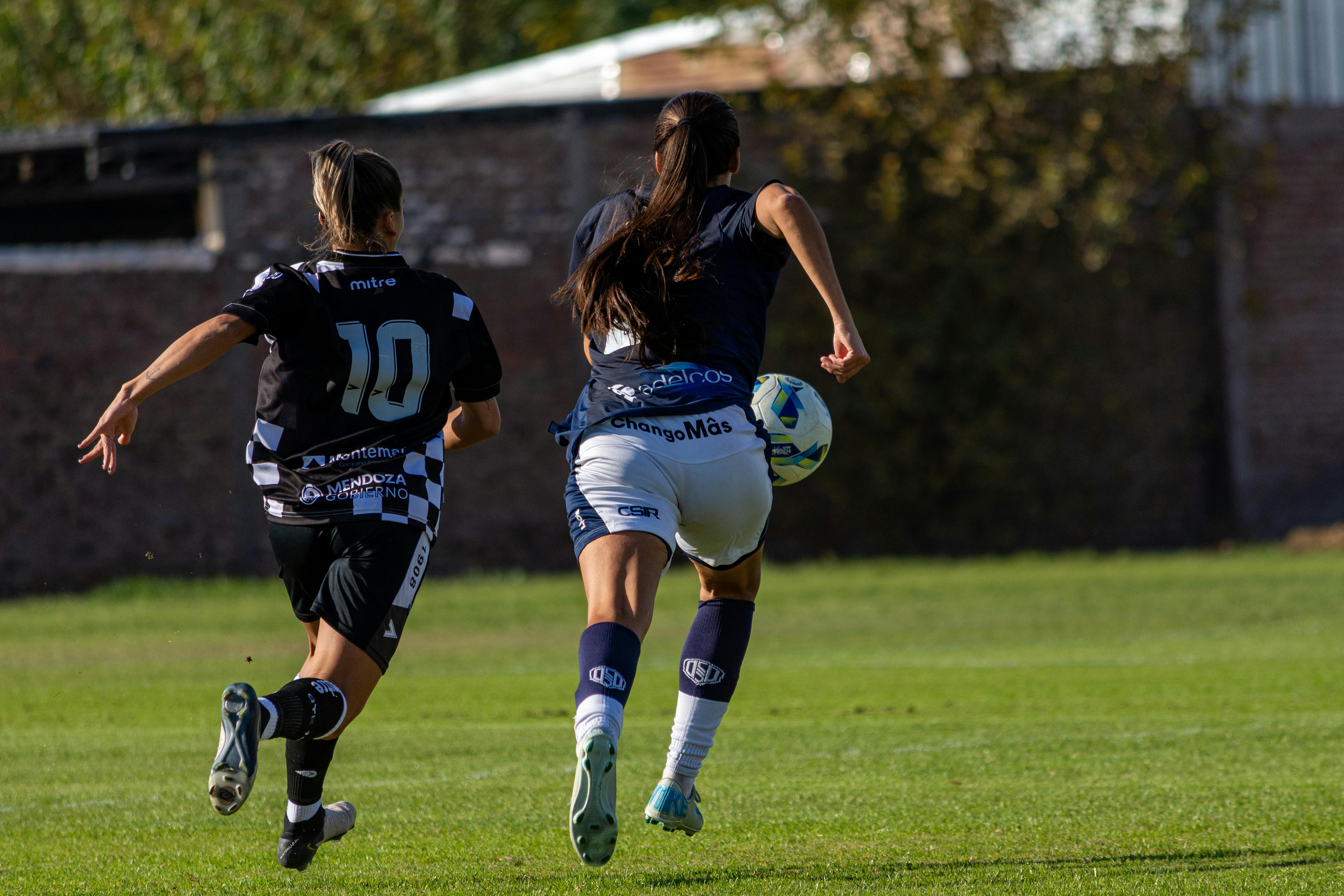 Exciting capture of two female soccer players in action on the field during a sunny day.