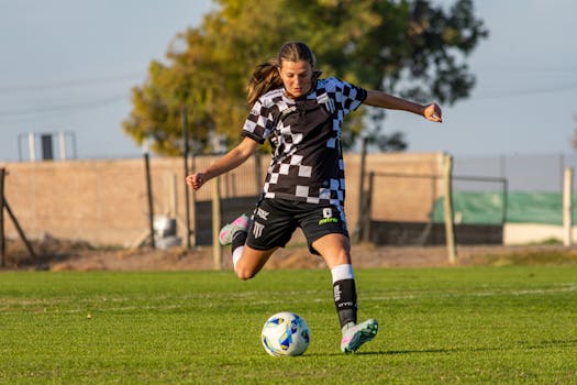 A female footballer in action, skillfully kicking a soccer ball on a sunny day outdoors.