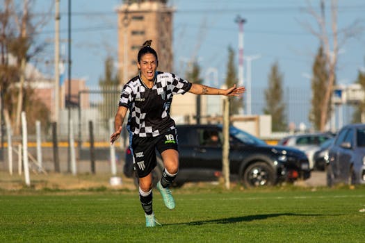 Excited female soccer player in black and white uniform celebrating a goal on the field outdoors.