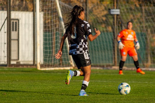 Dynamic shot of a female soccer player dribbling towards the goal on a sunny day match.
