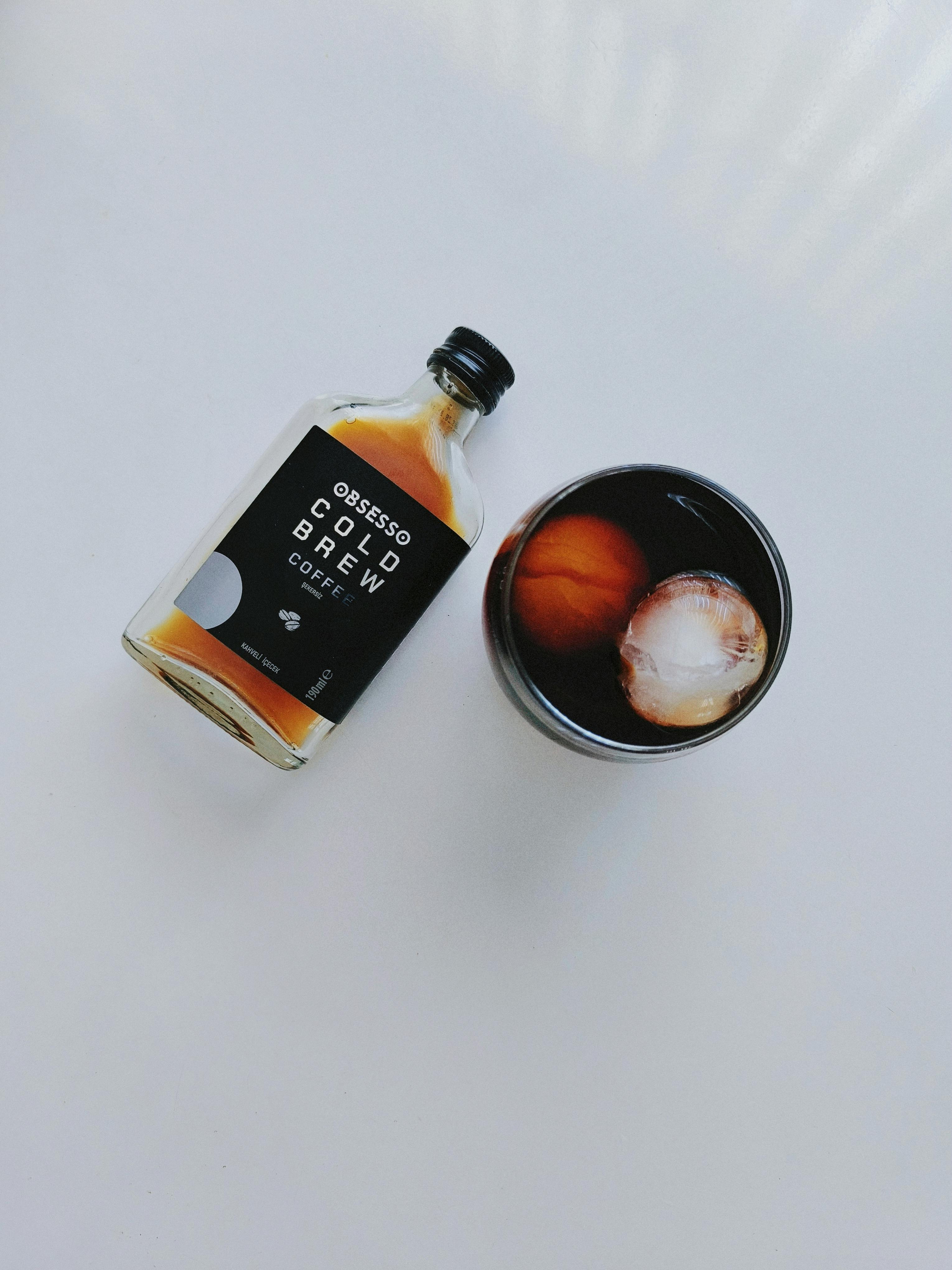 Cold brew coffee bottle and glass with ice on white background