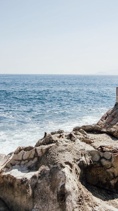 Free A serene view of waves hitting rocky cliffs under a clear sky. Stock Photo