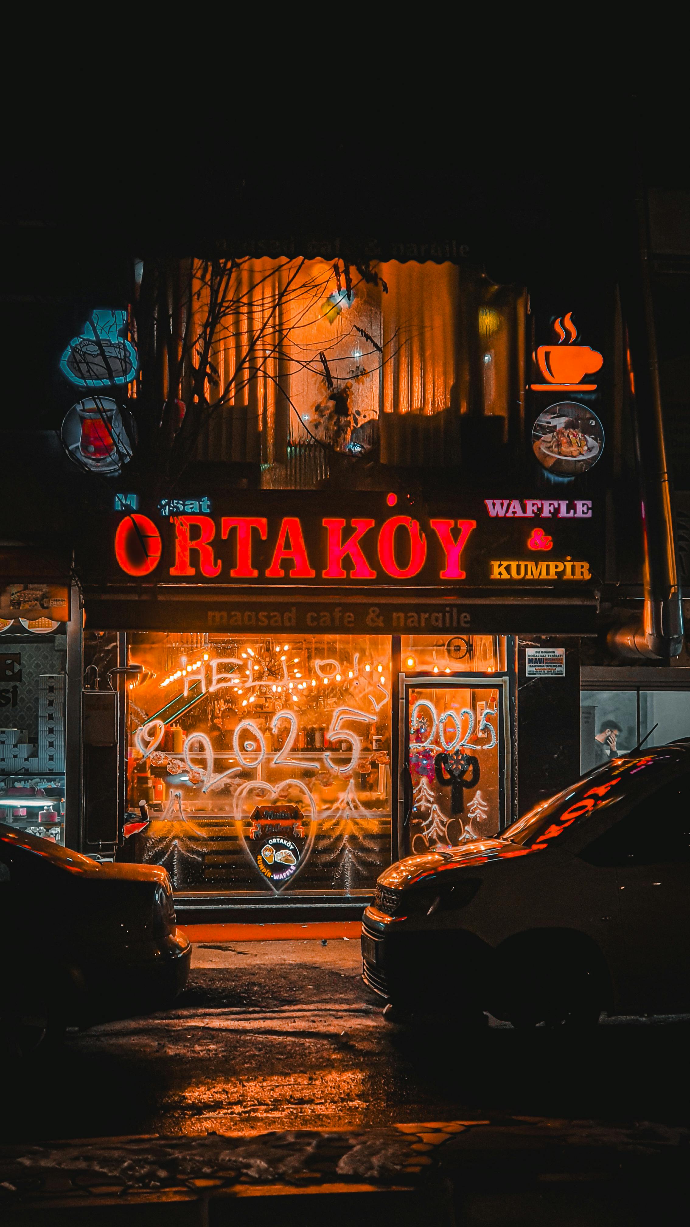 Vibrant neon signs illuminate Ortaköy cafe storefront at night, capturing urban nightlife essence.